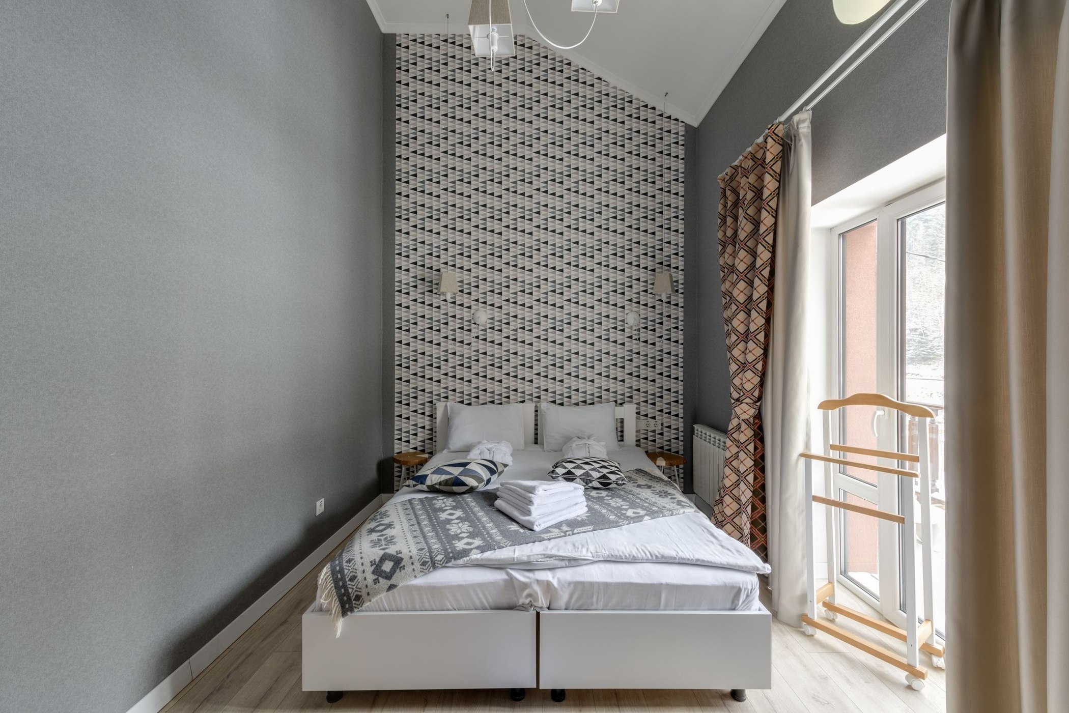 Repeating geometric wallpaper behind a double bed in a light hospitality interior