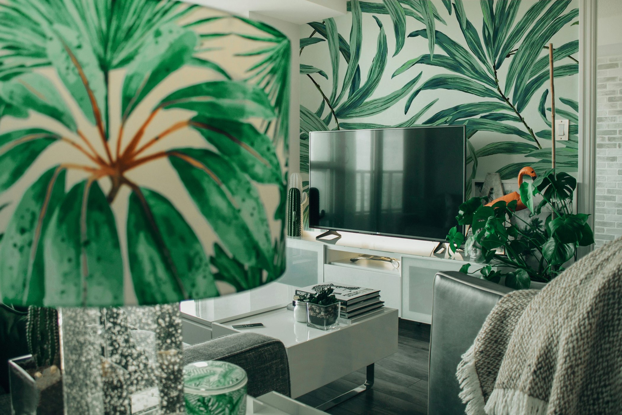 Large tropical leaf wallpaper beside a television in a finished living space